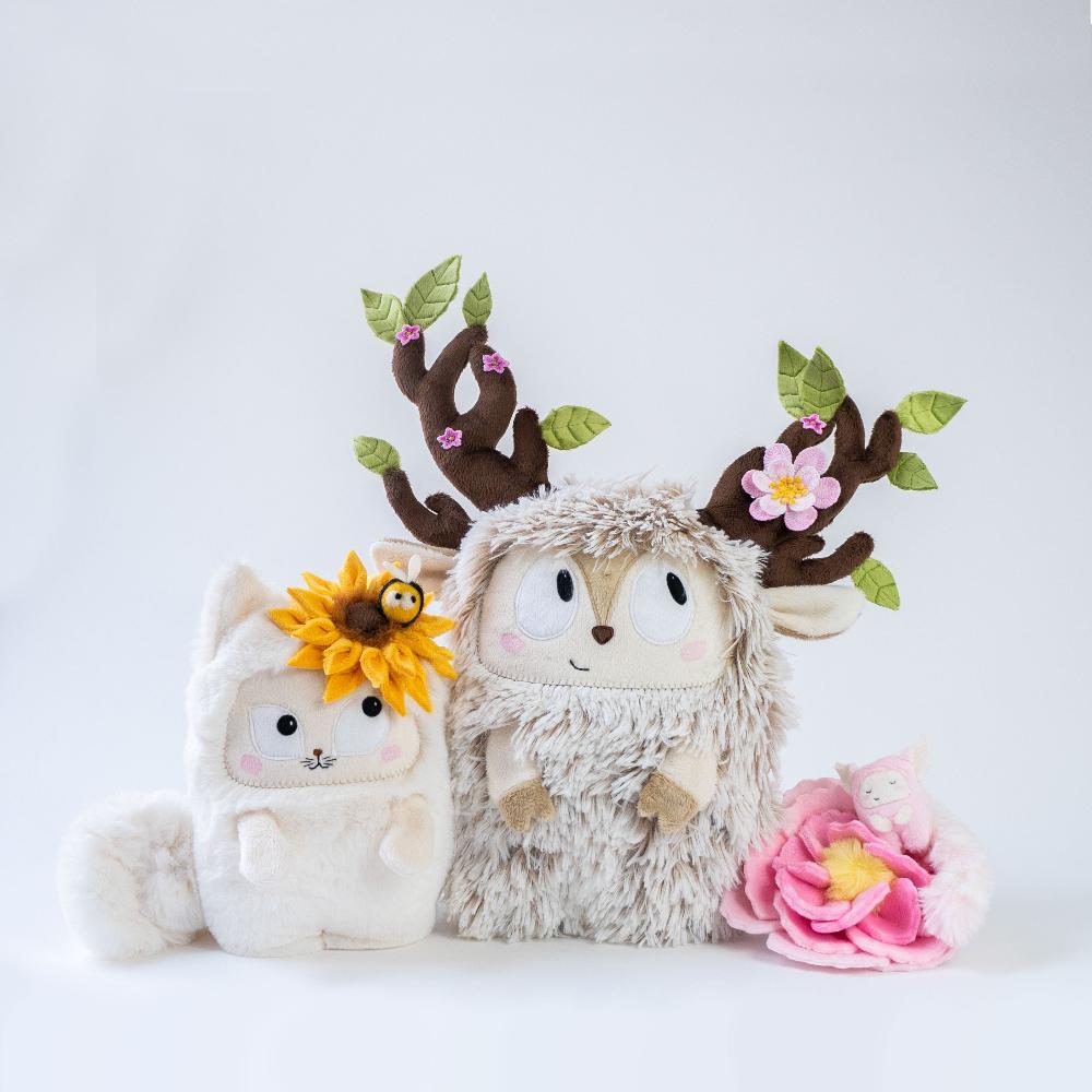 3 plush toys. A cat with a big sunflower, a deer with antlers covered with flowers and leaves, a tiny plush tiny sleeping plushie in a big flower